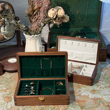 Wooden jewelry box with open compartments displaying jewelry on a floral-patterned surface.