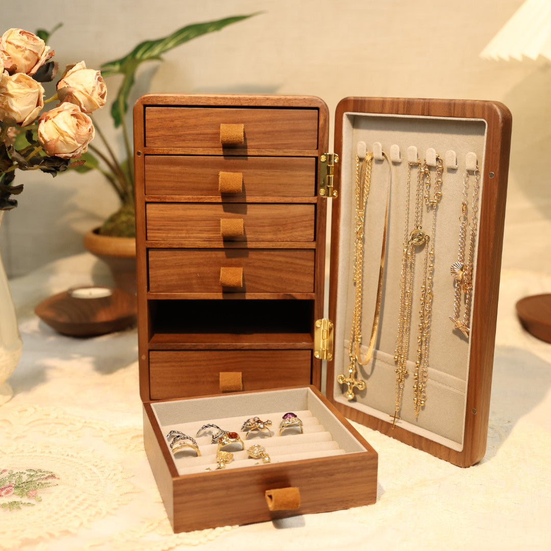 Wooden jewelry box with drawers and a display case on a table with decorative items.