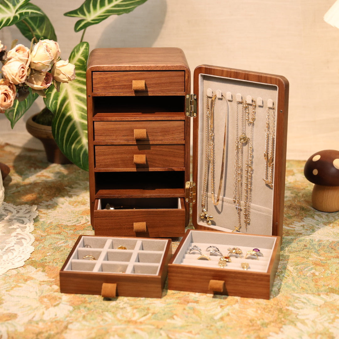 Wooden jewelry box with open drawers on a table with decorative items.