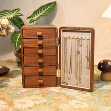 Wooden jewelry box with open lid displaying necklaces on a decorative table.