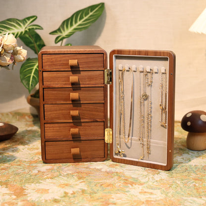Wooden jewelry box with open lid displaying necklaces on a decorative table.