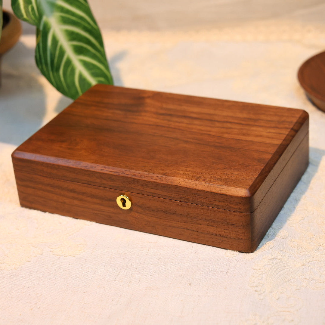 Wooden jewelry box on a textured surface with plants in the background