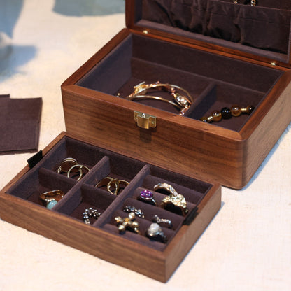 Wooden jewelry box with compartments containing jewelry on a light surface.