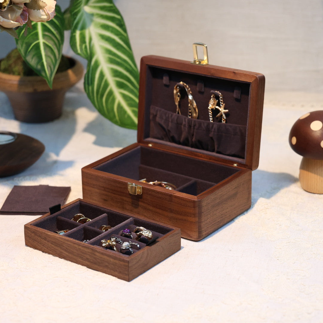Wooden jewelry box with jewelry on a light surface with plants in the background