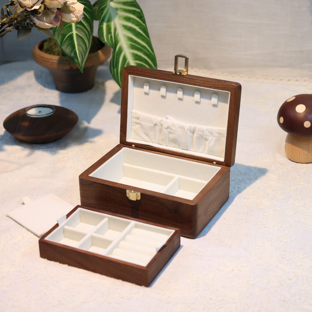 Wooden jewelry box with compartments on a light surface with decorative items.