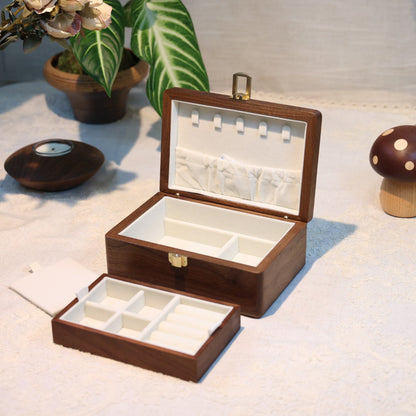 Wooden jewelry box with compartments on a light surface with decorative items.