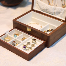 Wooden jewelry box with compartments containing earrings on a light surface