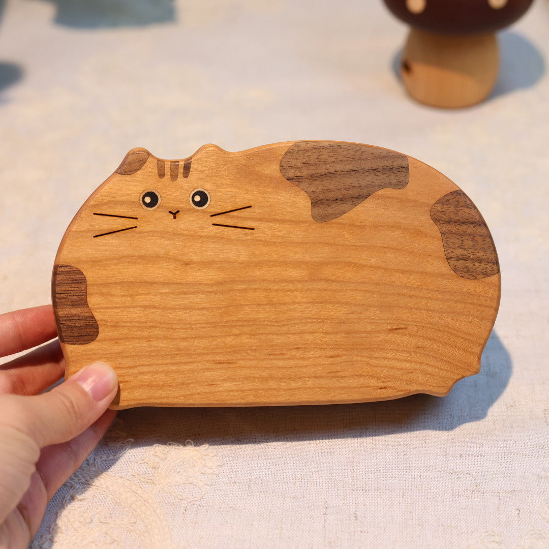 Wooden cat-shaped coaster held by a hand on a light surface
