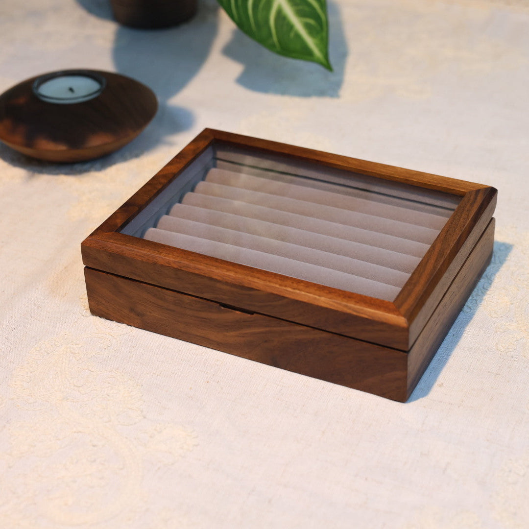 Wooden jewelry box on a textured surface with a plant in the background