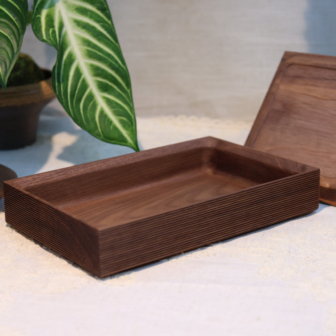 Wooden tray on a light surface with a plant and candle in the background