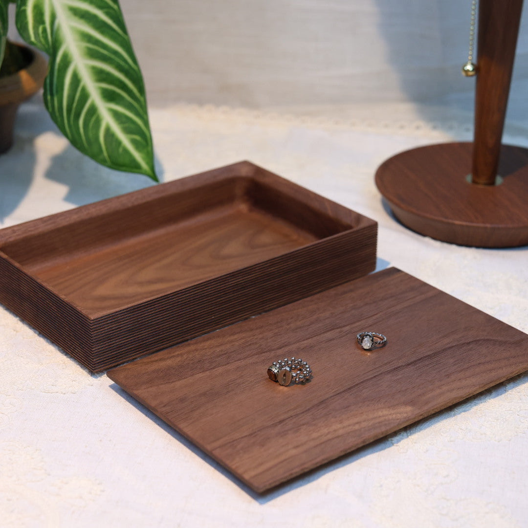 Wooden jewelry box with a small heart-shaped object on a light surface with plants in the background.