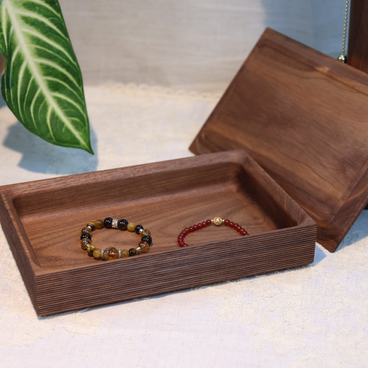 Wooden jewelry box with bracelets on a light surface, plant and candle in the background