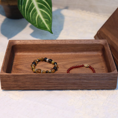 Wooden tray with beaded bracelets on a light surface with a plant in the background