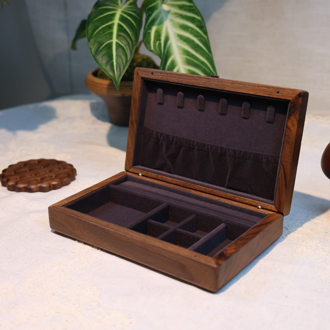 Wooden jewelry box with compartments on a textured surface with plants in the background