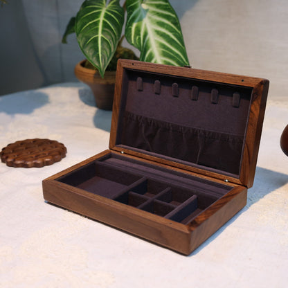 Wooden jewelry box with compartments on a textured surface with plants in the background