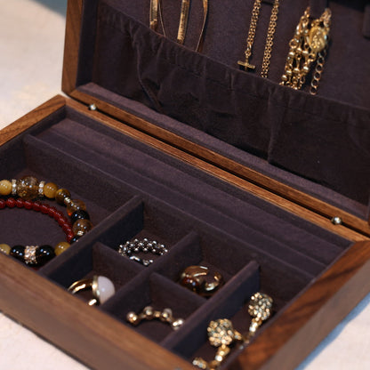 Wooden jewelry box with compartments containing various jewelry items on a light surface.
