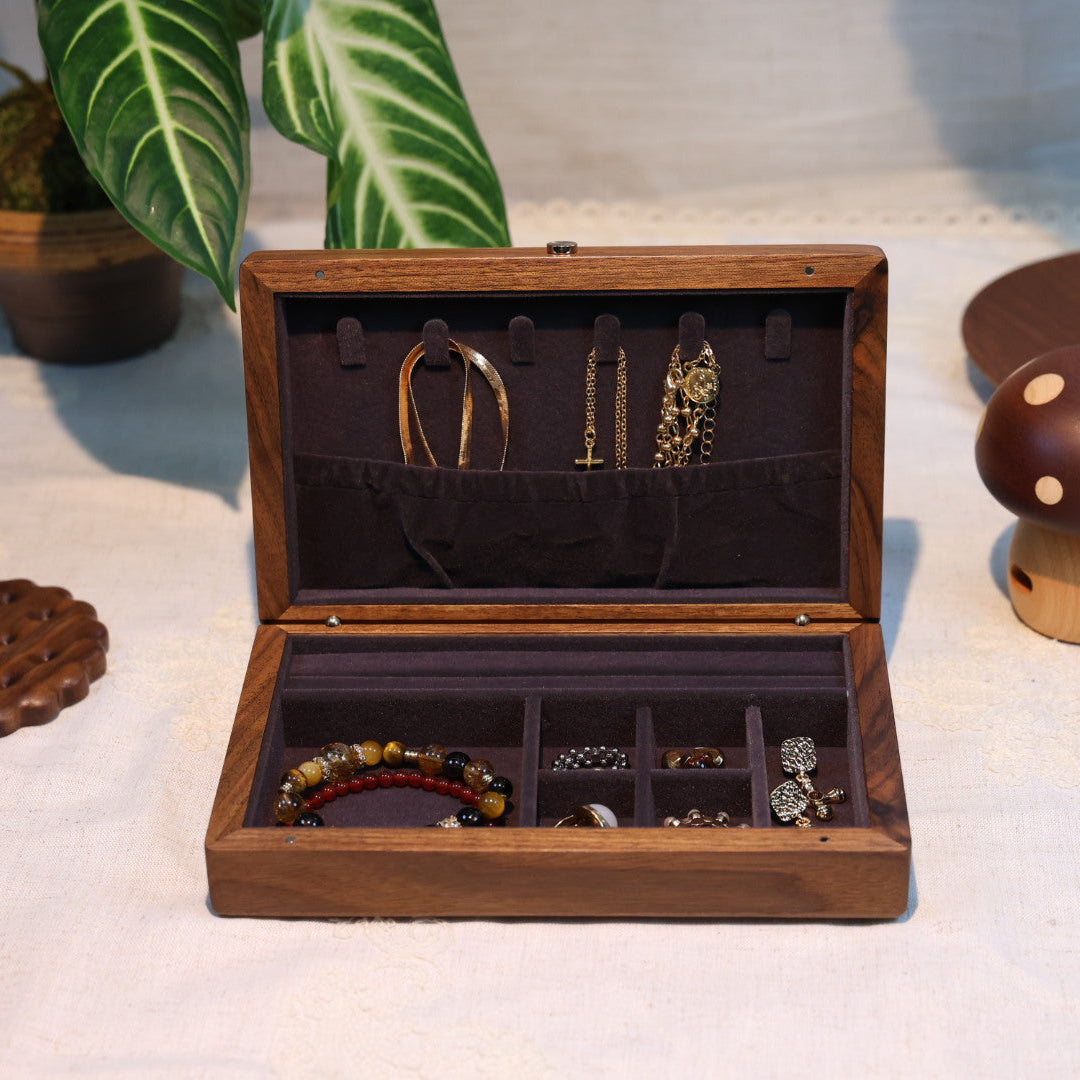 Wooden jewelry box with jewelry inside on a light surface with plants in the background