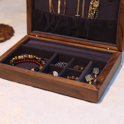 Wooden jewelry box with compartments containing various jewelry items on a light background