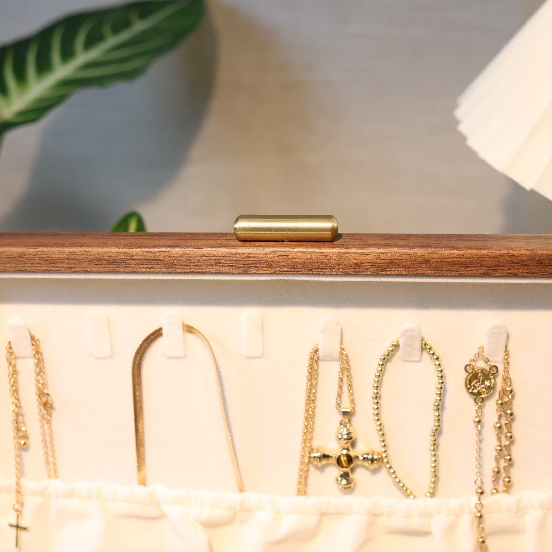 Wooden jewelry box with gold necklaces and earrings on a neutral background