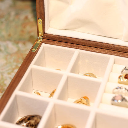 Wooden jewelry box with compartments containing various pieces of jewelry on a floral-patterned surface.