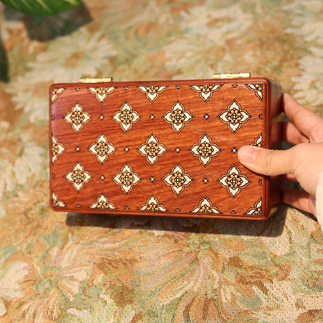 Wooden box with decorative patterns held by a hand on a floral-patterned surface