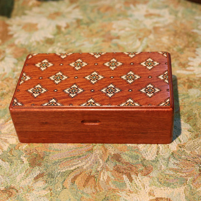 Wooden jewelry box with decorative inlay on a floral-patterned fabric background
