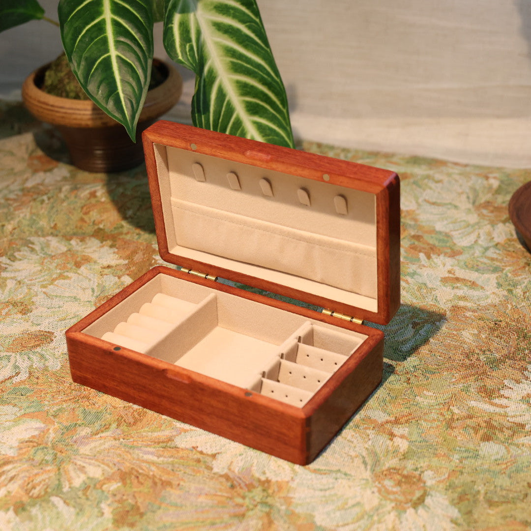 Wooden jewelry box on a patterned surface with plants in the background