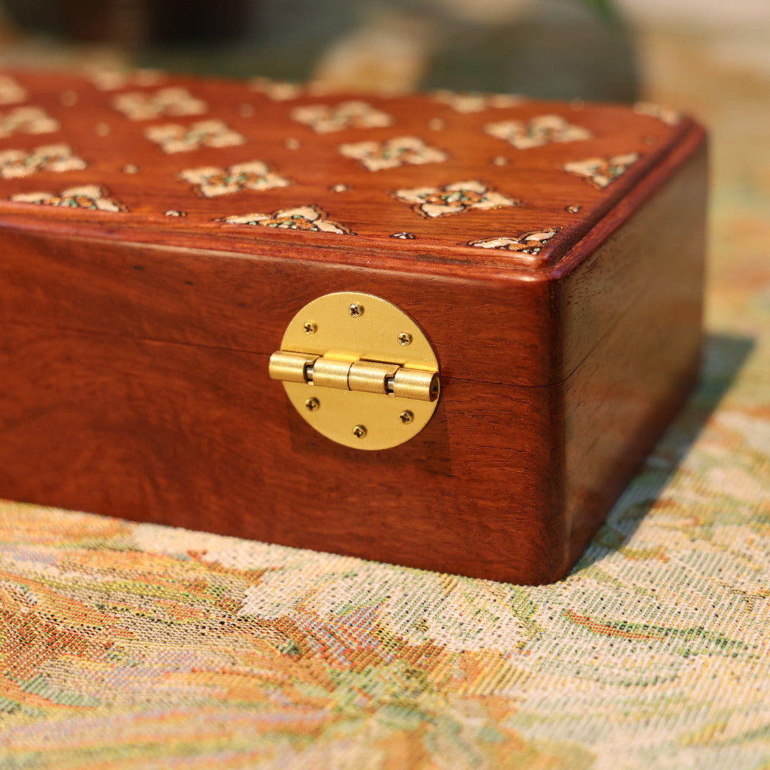 Wooden jewelry box with brass hinges on a patterned fabric background