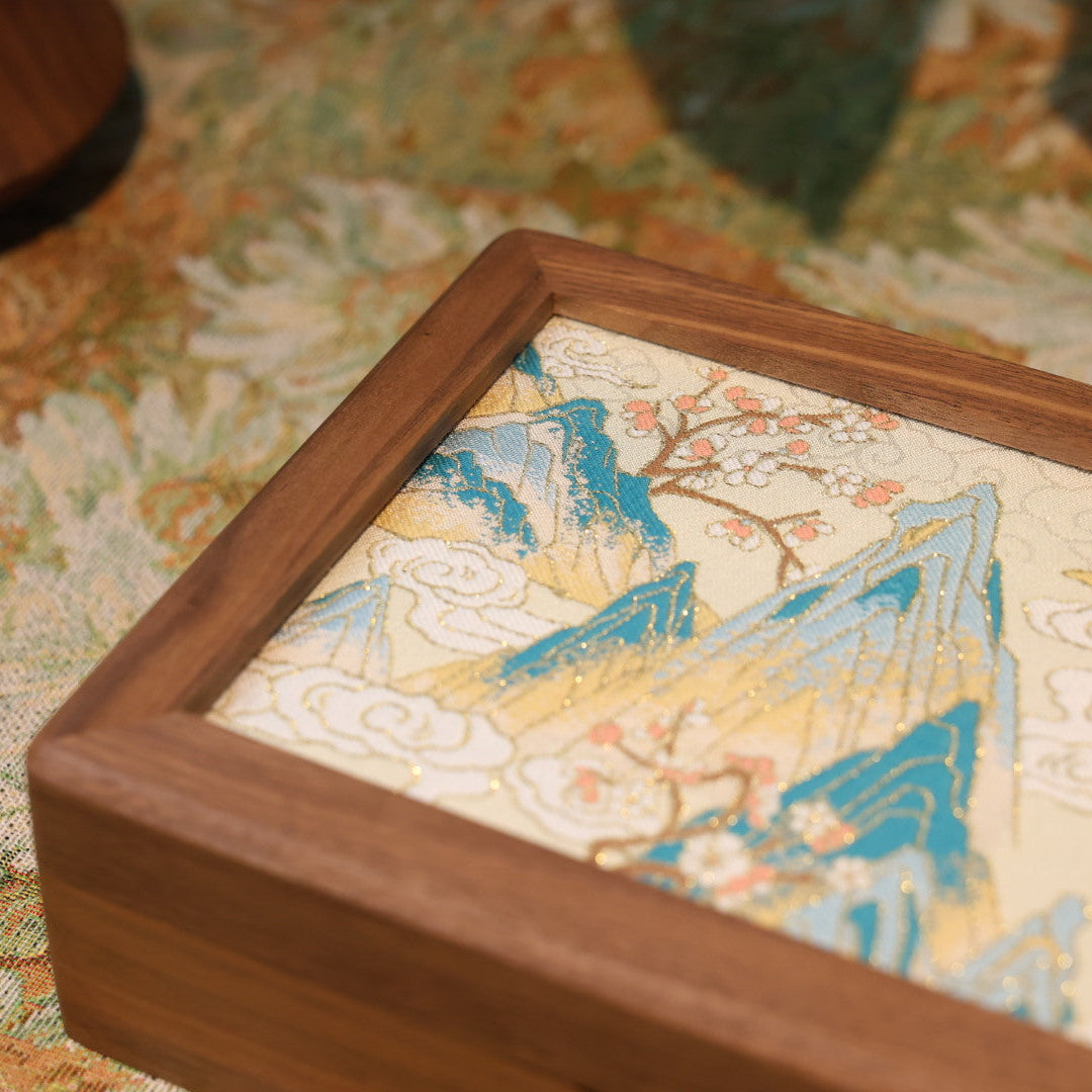 Wooden frame with embroidered fabric featuring a landscape design on a floral-patterned surface.