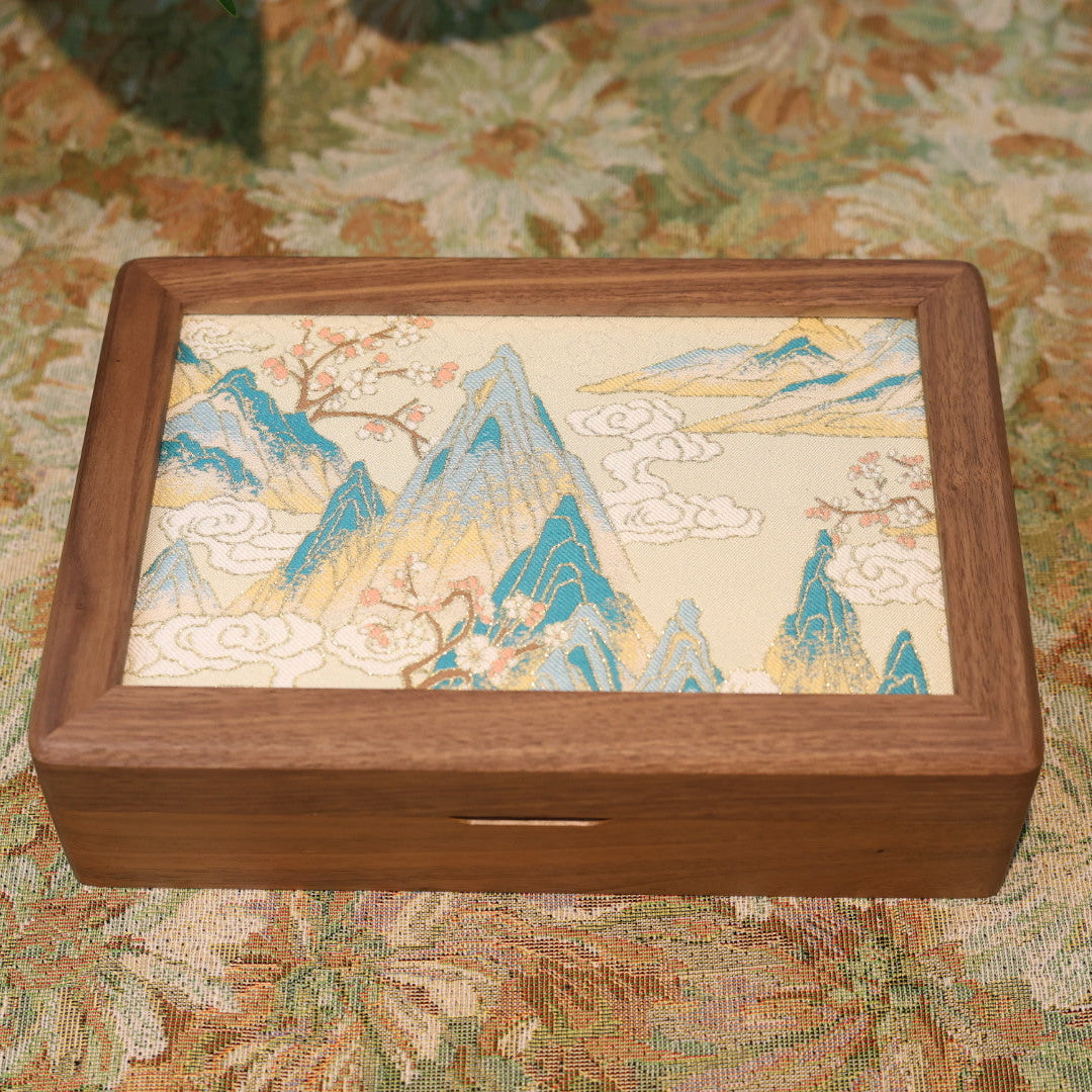 Wooden box with a decorative lid featuring mountain and landscape design on a floral-patterned surface.