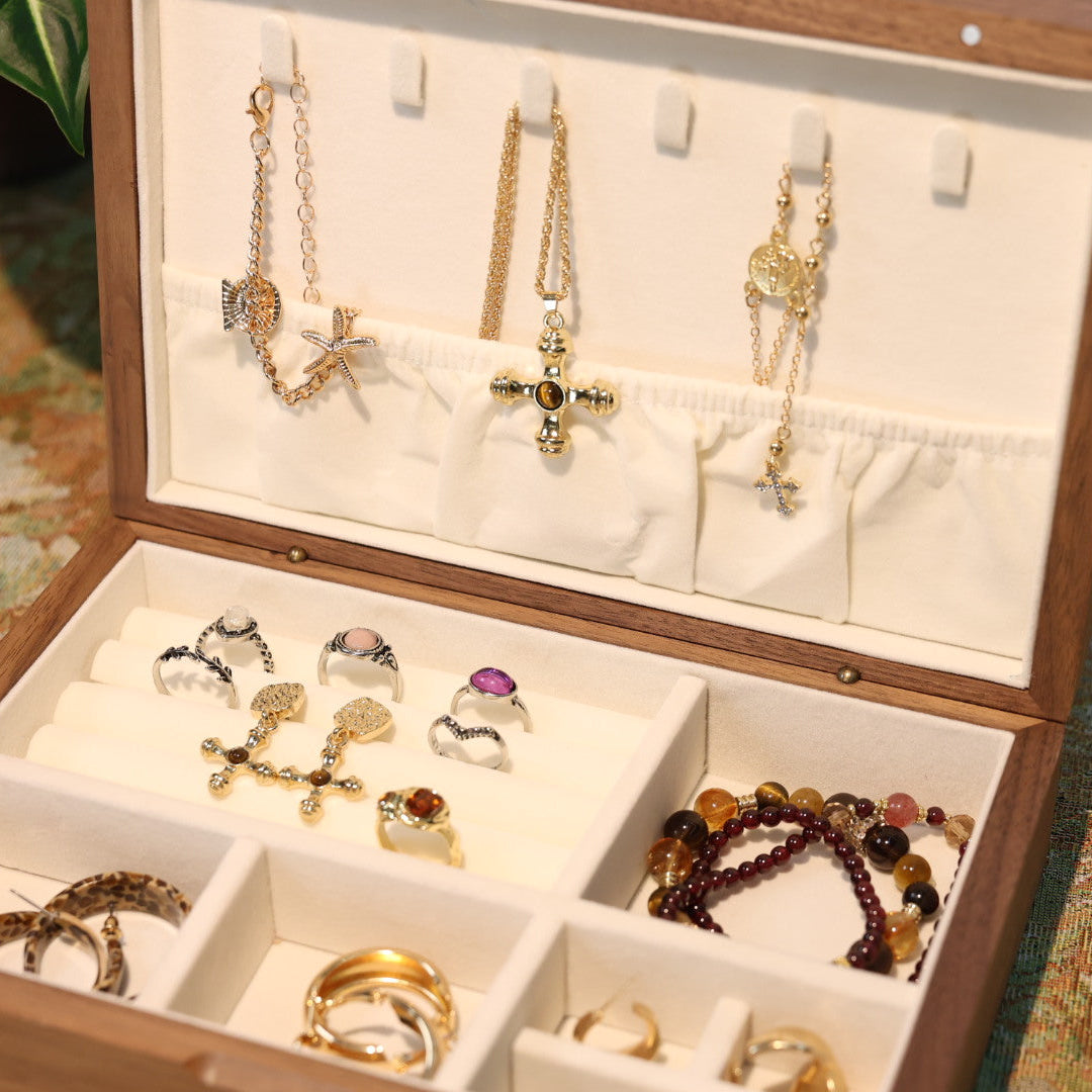 Wooden jewelry box with various necklaces, rings, and bracelets displayed on a patterned surface.