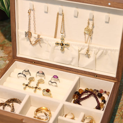 Wooden jewelry box with various necklaces, rings, and bracelets displayed on a patterned surface.