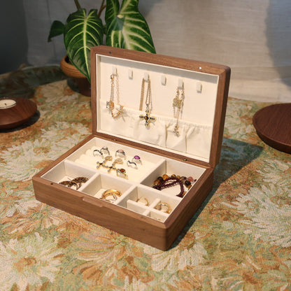 Wooden jewelry box with jewelry on a floral-patterned tablecloth.