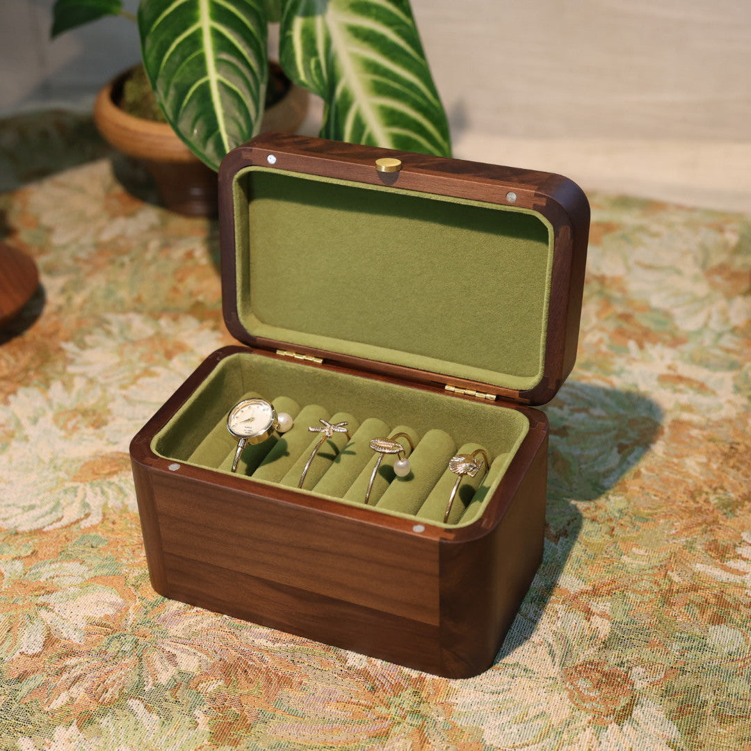 Wooden jewelry box with green interior containing earrings on a patterned surface.