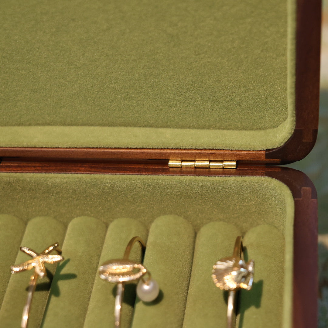 Gold earrings in a green jewelry box on a textured surface