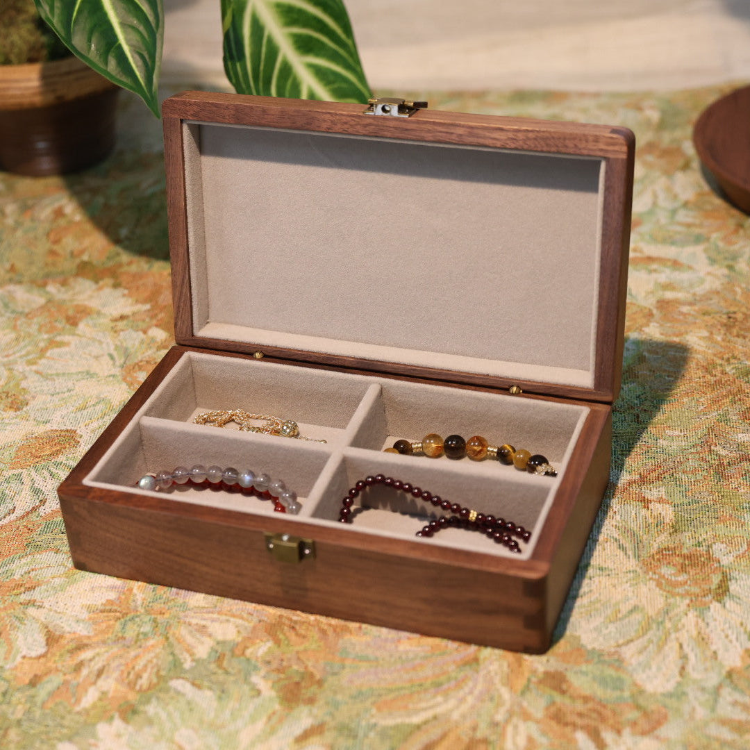Wooden jewelry box with compartments containing bracelets on a floral-patterned surface.