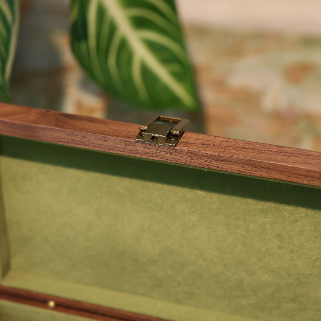 Wooden jewelry box with green interior, blurred plant in the background