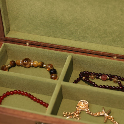 Open jewelry box with green interior containing three beaded bracelets and a gold necklace.