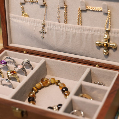 Open jewelry box with various necklaces, rings, and a bracelet on a patterned surface.