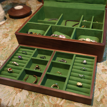 Jewelry box with green interior compartments filled with various rings on a patterned surface.