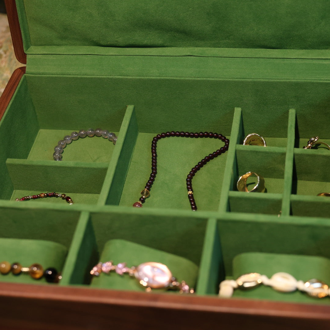 Jewelry box with compartments containing various pieces of jewelry on a textured surface.