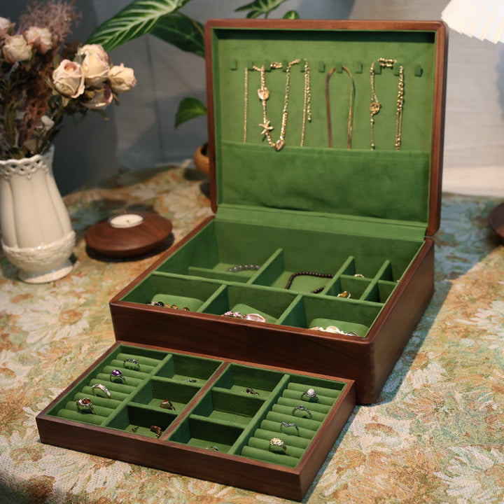 Open jewelry box with green interior displaying various necklaces on a patterned tablecloth.