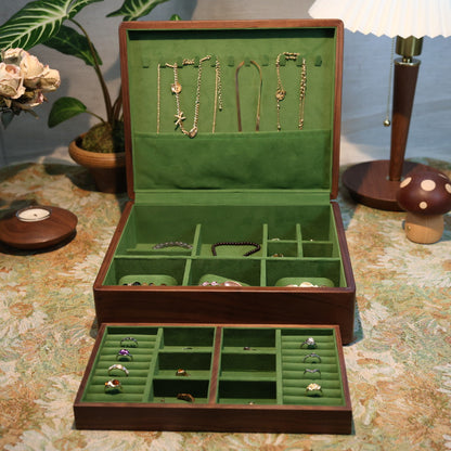 Open jewelry box with green interior displaying various jewelry items on a patterned surface.