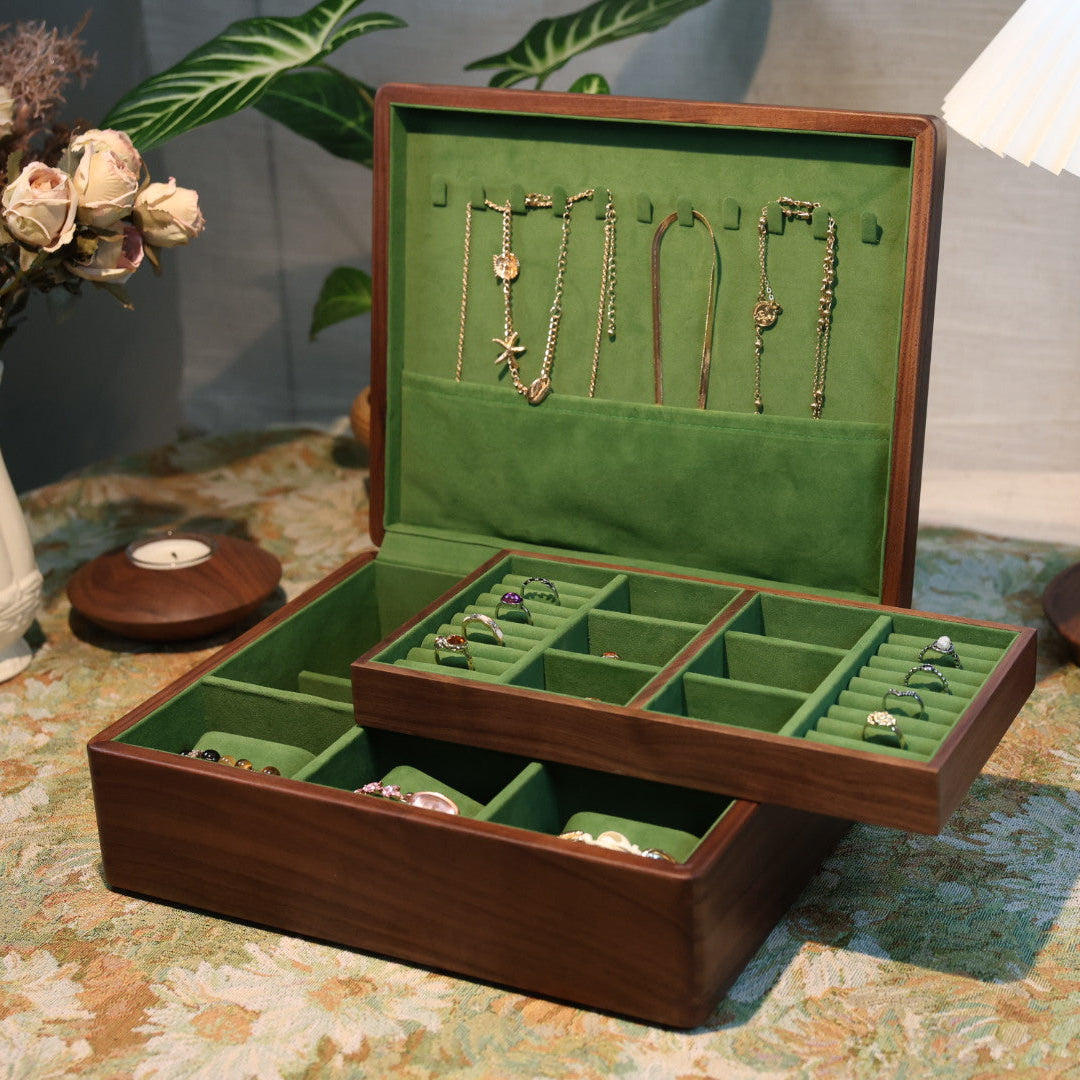 Jewelry box with green interior containing necklaces on a patterned tablecloth.