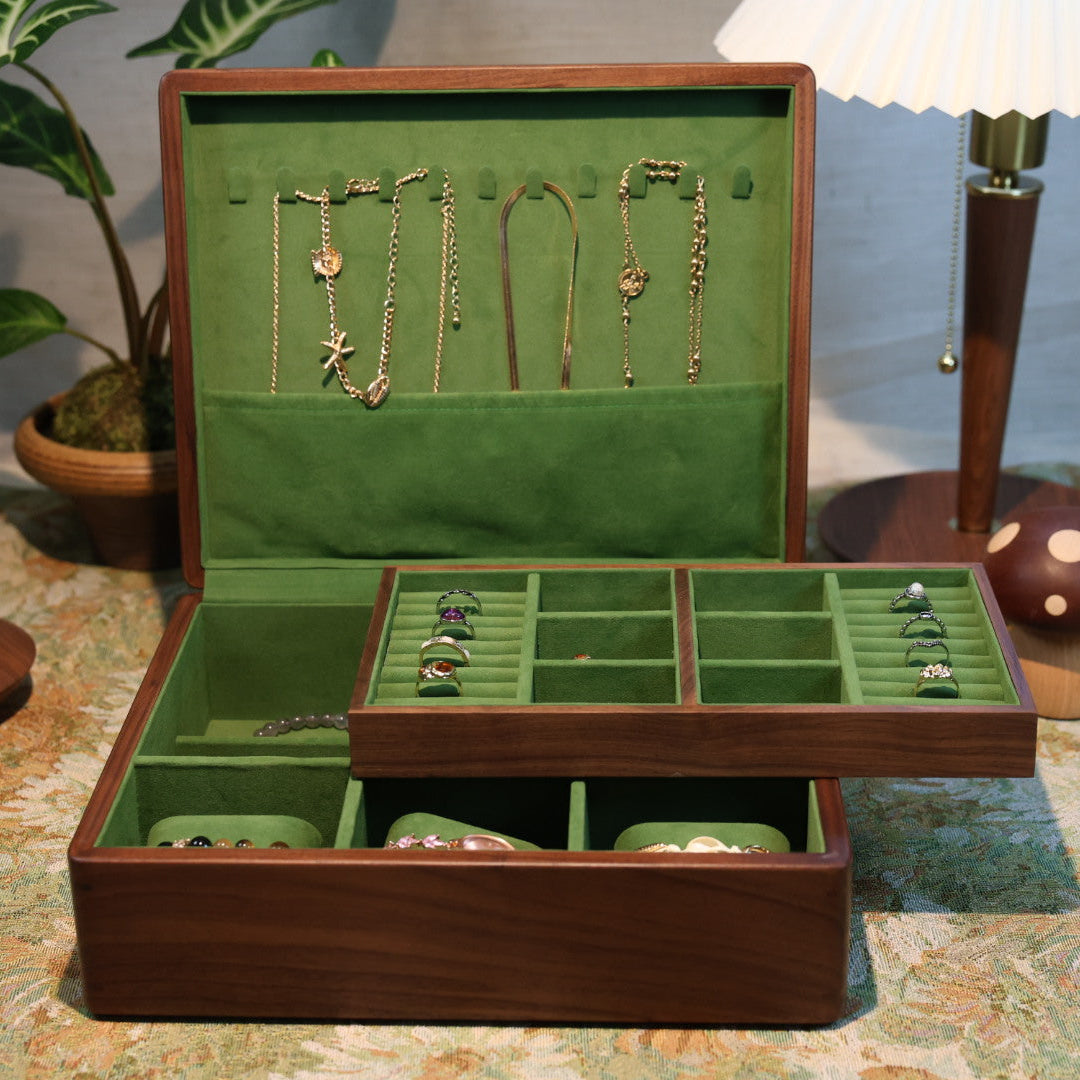 Open jewelry box with green interior displaying necklaces on a patterned surface.