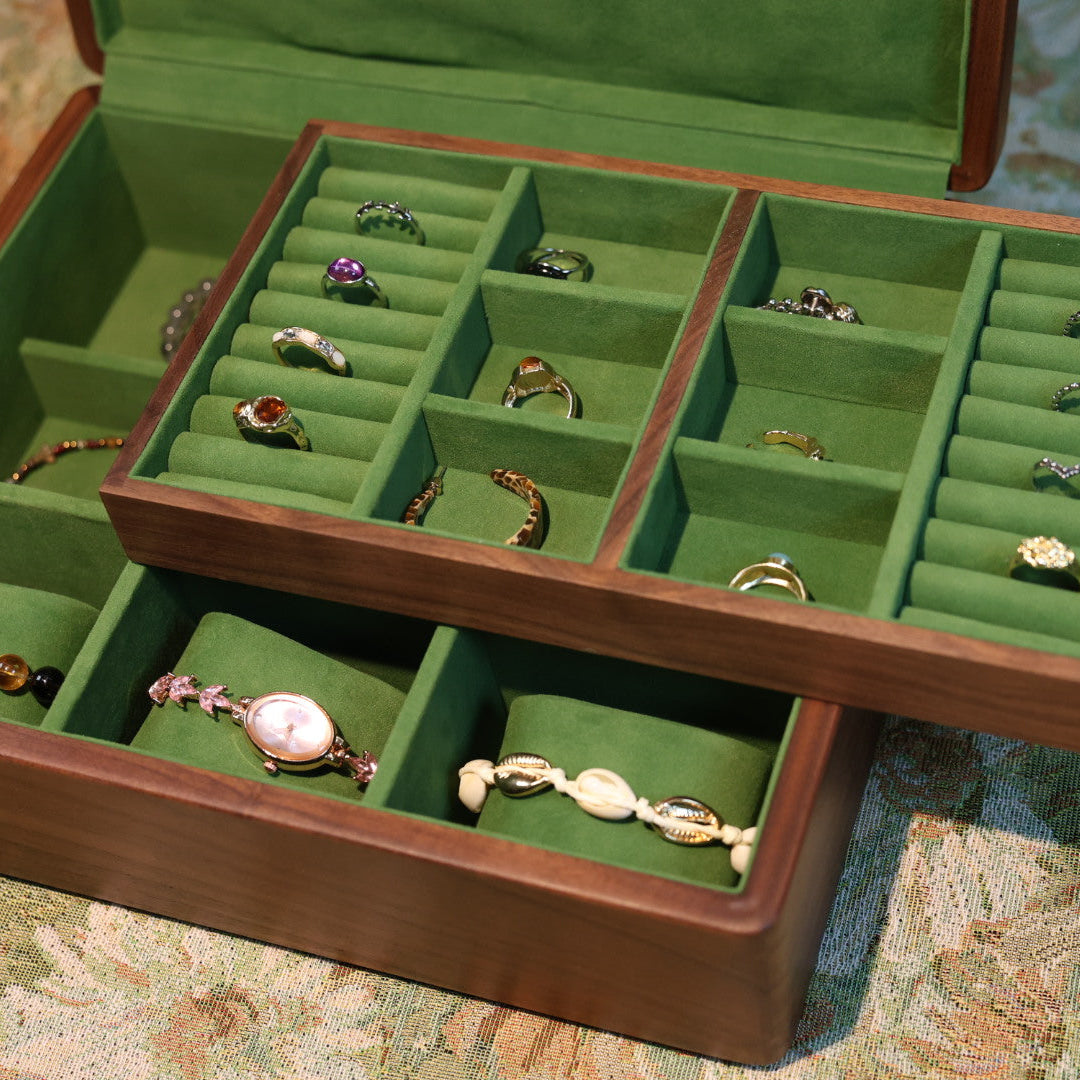 Wooden jewelry box with green interior holding various rings on a patterned surface.
