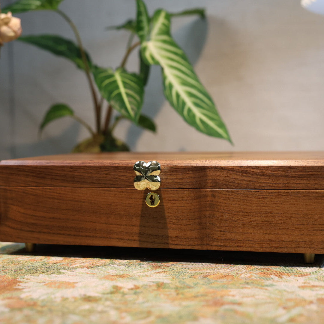 Wooden jewelry box with a gold clasp on a patterned surface with plants in the background