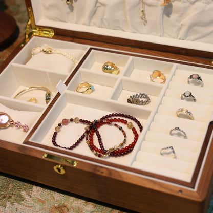 Wooden jewelry box with compartments containing various pieces of jewelry on a patterned surface.