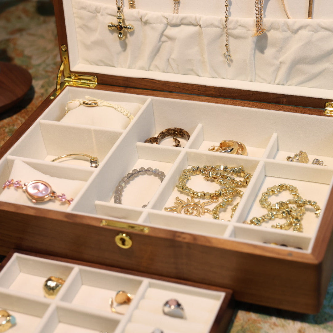 Wooden jewelry box with compartments filled with various pieces of jewelry on a patterned surface.