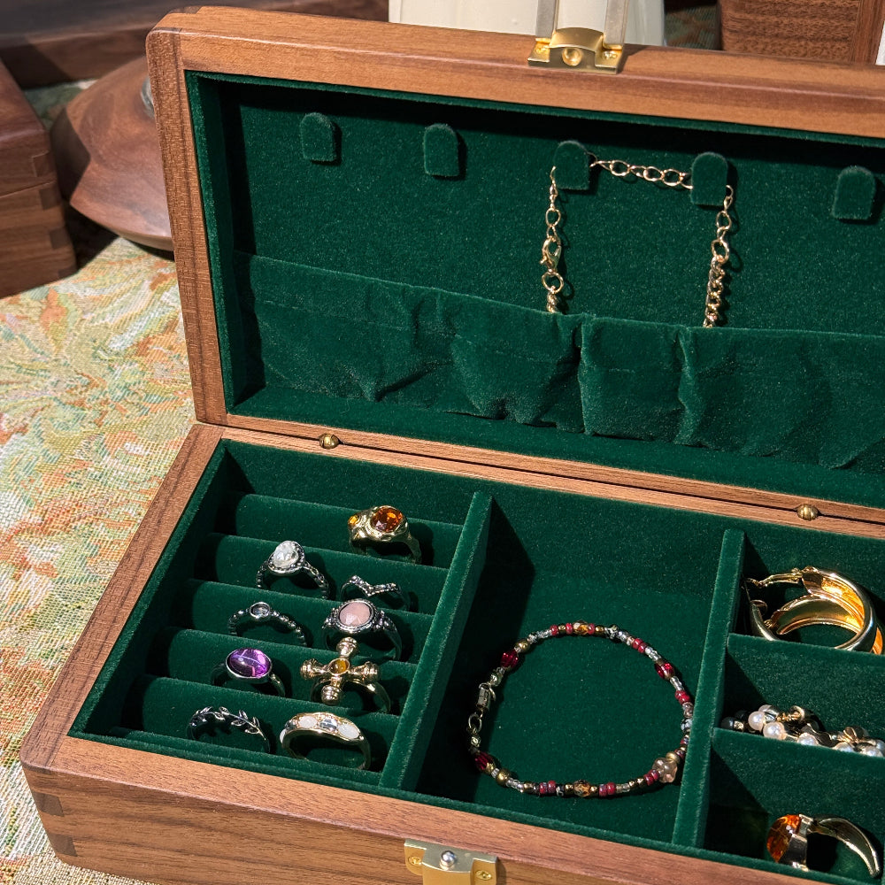 Open jewelry box with green interior displaying various jewelry items.